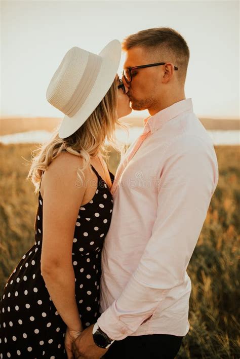 A Man With A Woman In A Hat Hug And Kiss In The Tall Grass In The Meadow Stock Image Image Of