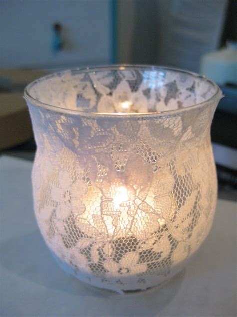 A Lit Candle In A Glass Vase On A White Tablecloth With Lace Doily