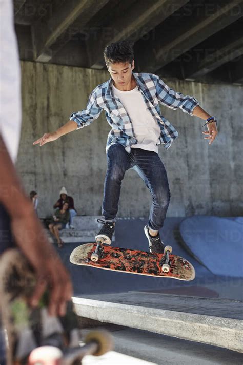 Focused Teenage Boy Flipping Skateboard At Skate Park Stock Photo