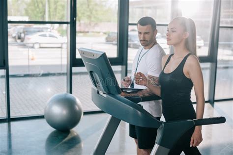 Male Personal Trainer Looking At Treadmill Screen While Sportswoman