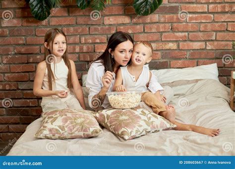 Mom Sits On The Bed With Her Son And Babe And Watch A Movie A Woman A Babe And A Girl Eat