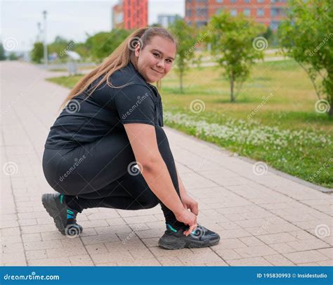 a fat woman in a tracksuit crouches down and ties her shoelaces outdoors stock image image of