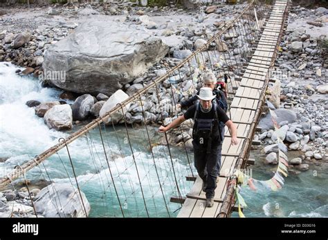Trekkers Crossing A Suspension Bridge Crossing On The Annapurna Base