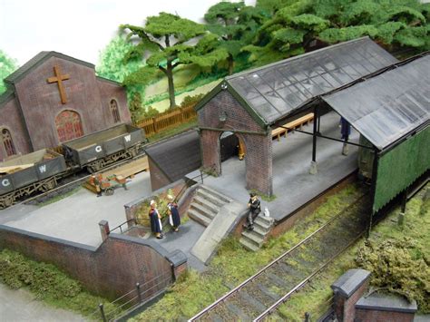 A Model Train Station With People Standing On The Platform Next To It
