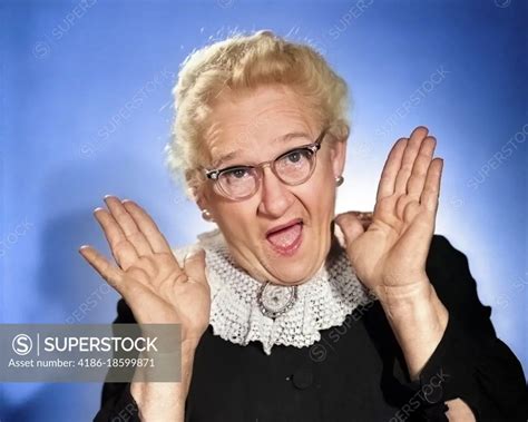 S Elderly Woman In Granny Glasses Holding Hand Up Near Face With Mouth Open Looking At