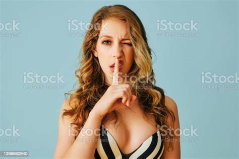 Beautiful Young Adult Woman With One Eye Closed And Long Curly Hair And Finger On Lips Sharing