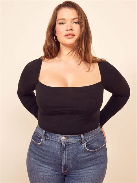 A Woman In Jeans And A Black Top Poses For The Camera With Her Hands On