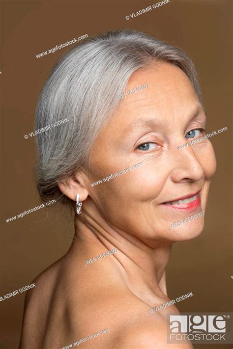 Portrait Of Naked Senior Woman With Grey Hair In Front Of Brown