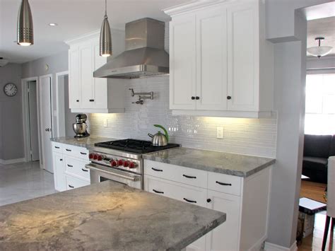 White and grey kitchen with yellow accents features white cabinets paired with statuary marble countertops fitted with a stainless steel integrated cooktop and a dark grey tiled backsplash, walker zanger 6th avenue cocoon tiles, under a gray vent hood flanked by stacked white floating shelves. Custom Kitchen Countertops Granite Laminate Quartz Marble Counter Tops Kitchen Renovations ...