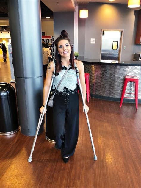 A Woman With Two Crutches Is Standing In An Airport Lobby And Smiling At The Camera