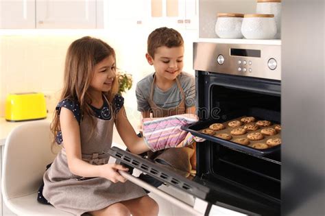 Cute Children Taking Cookies Out Of Oven In Kitchen Cooking Pastry