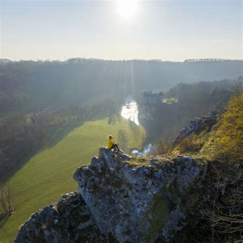 Aerial View Of A Woman Sitting On The Rocks With Walzin Castle In Background At Sunset Dinant