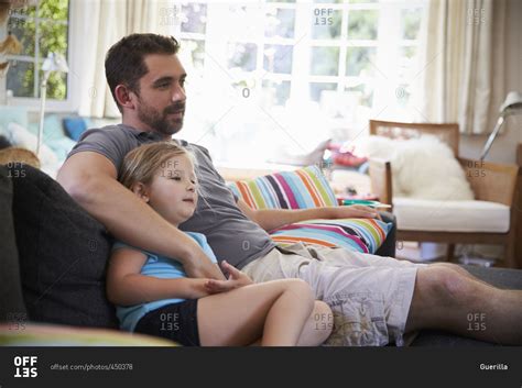 Father And Daughter Sitting On Sofa Watching Tv Together Stock Photo