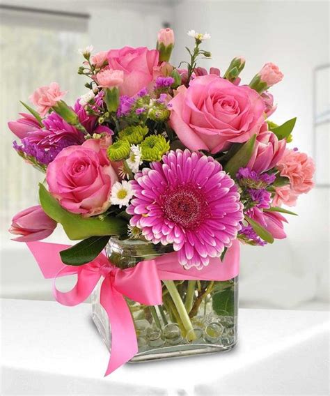 A Vase Filled With Pink And Purple Flowers On Top Of A White Tablecloth Next To A Window