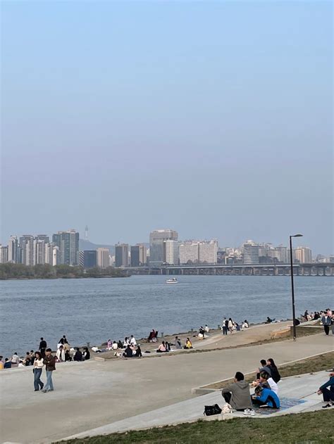 Many People Are Sitting On The Grass Near The Water And In The Distance