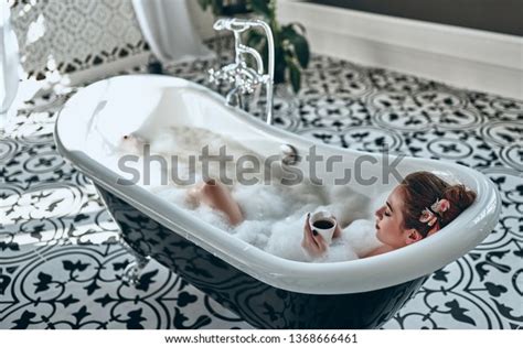Attractive Sexy Woman Lying Naked In Bath Full Of Foam With Cup Of Tea In Modern Bathroom
