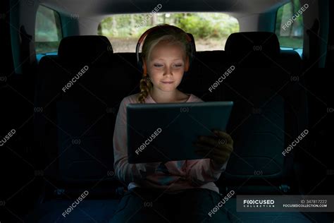 mädchen mit kopfhörer und digitalem tablet auf dem rücksitz des autos — film dreiviertelansicht