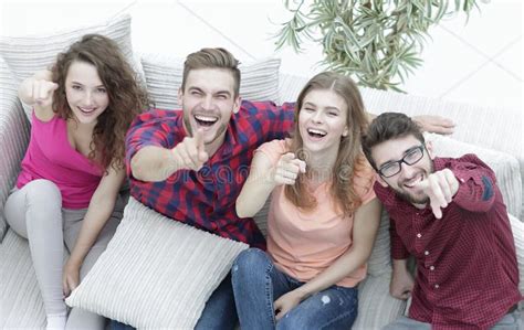 Group Of Laughing Friends Sitting On Sofa And Showing Forefinger On The