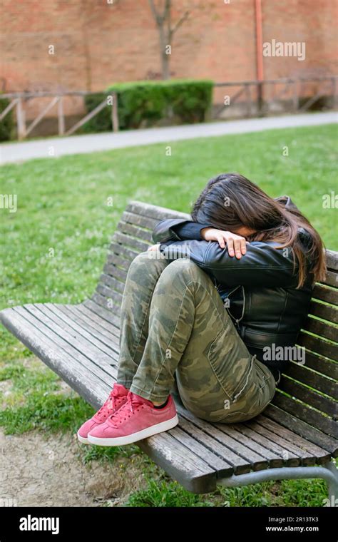 Young Woman Sad And Depressed Situated On Park Bench With Arms And Head