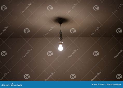 Naked Lit Light Bulb Hanging From The Ceiling Of A Dimly Lit Room Stock Photo Image Of