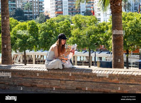 Young Female Spanish Tourist Looking At Map Of Seville Sitting Near The River Guadalquivir Stock