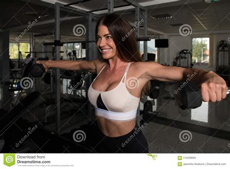 Woman Exercising Shoulders With Dumbbells In The Gym Stock Photo