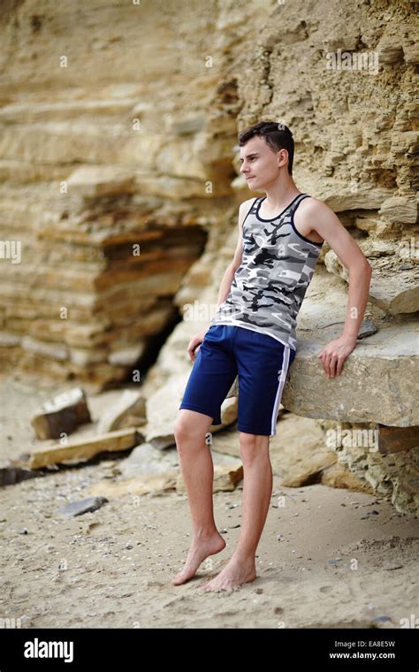 Teenage Boy Barefoot Sitting On The Rocks On A Cliff At The Seaside