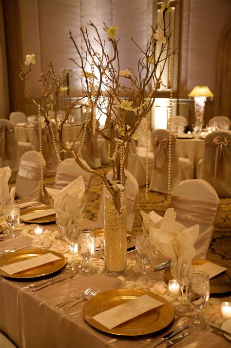 The Table Is Set With White Linens Gold Plates And Flowers In Vases