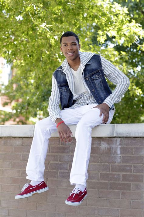 A Man Sitting On Top Of A Brick Wall Wearing White Pants And A Jean Vest