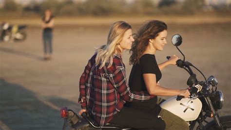 Beautiful Young Woman Motorcyclist With His Girlfriend Riding A Motorcycle In A Desert On Sunset