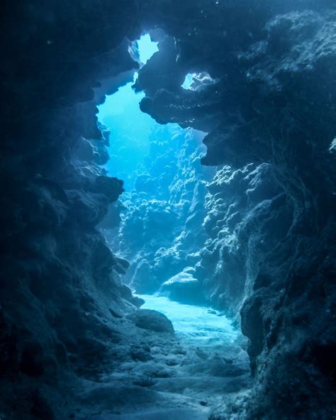 An Underwater Cave With Blue Water And Rocks On The Bottom Looking