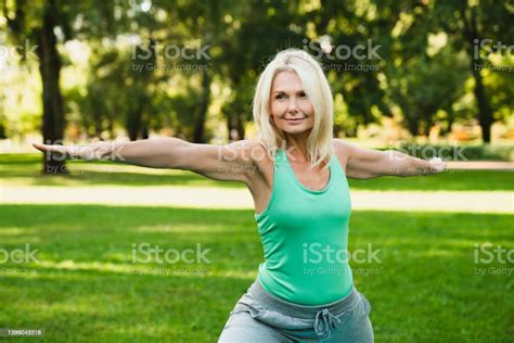 Beautiful Mature Fit Woman In Fitness Outfit Doing Physical Exercises In Public Park Stretching