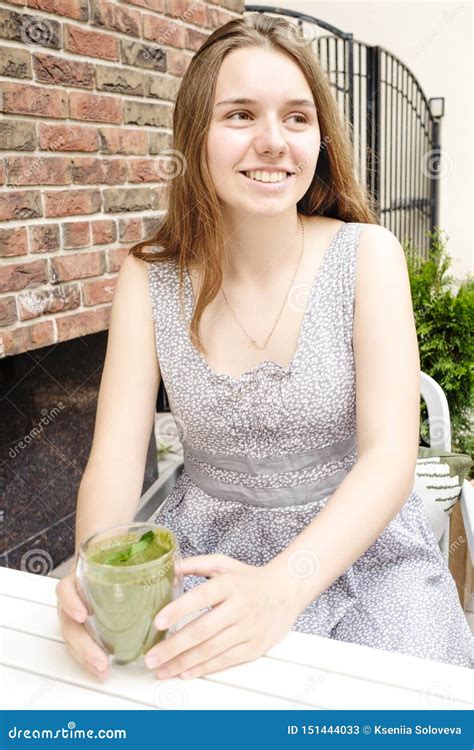 A Young Girl In An Outdoor Cafe Is Drinking A Green Smoothie And Smiling The Concept Of Healthy