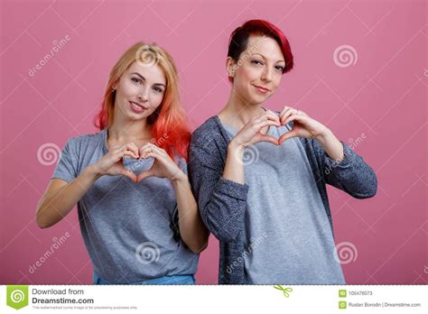 Dos Lesbianas Con Sonrisas Se Colocan De Lado A Lado En Un Fondo Rosado Imagen De Archivo