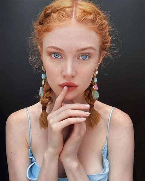 A Woman With Red Hair And Blue Eyes Is Posing For The Camera While Holding Her Finger To Her Mouth