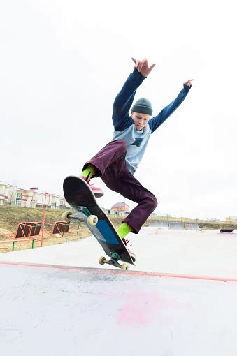 A Skateboarder Teenager In A Hat Does A Trick With A Jump On The Ramp A