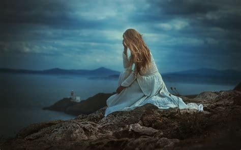 Фото Девушка в белом платье сидит на скале на фоне моря и смотрит вдаль фотограф TJ Drysdale