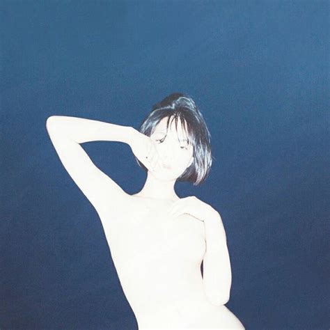 A Naked Woman Standing In Front Of A Dark Blue Background With Her Hand On Her Head