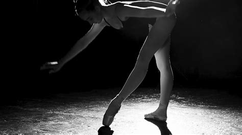cute flexible ballerina standing on her pointe ballet shoes in spotlight on black background in