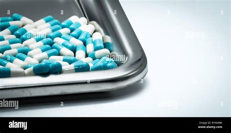Blue-white capsule pills on stainless steel drug tray. Pharmaceutical