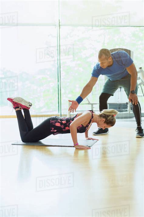 Personal Trainer Guiding Woman Doing Push Ups On Knees At Gym Stock