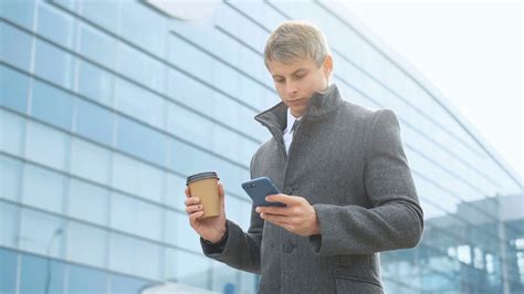 Portrait Of Serious Businessman Texting On A Mobile Cell Phone And Holding A Cup Of Coffee