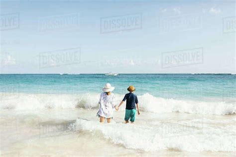 Mother And Son Holding Hands Standing In Surf On Beach Rear View