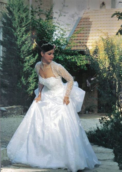 A Woman In A White Wedding Dress Is Standing Outside