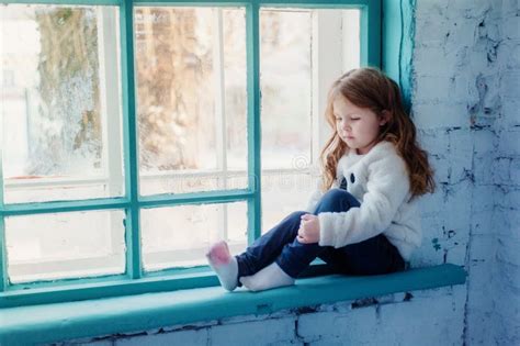 Little Girl Sitting On The Windowsill Near The Window Stock Image