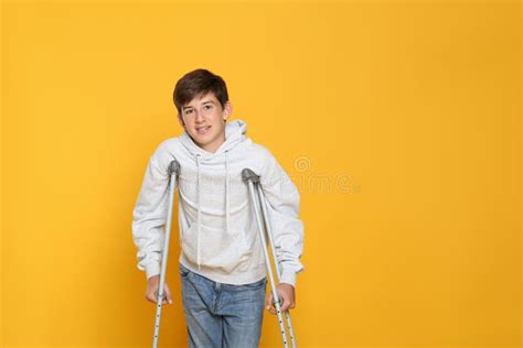 Teenage Boy With Injured Leg Using Crutches On Yellow Background Space