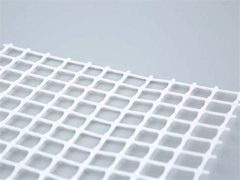 A Piece Of White Plastic Mesh With Large Square Meshes On The Gray