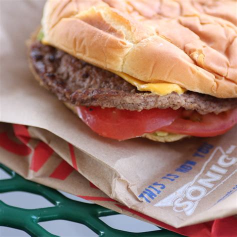 A Close Up Of A Hamburger On A Bun With Cheese And Tomatoes In Paper