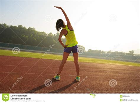Woman Runner Stretching Before Run During Sunny Morning On Stadium