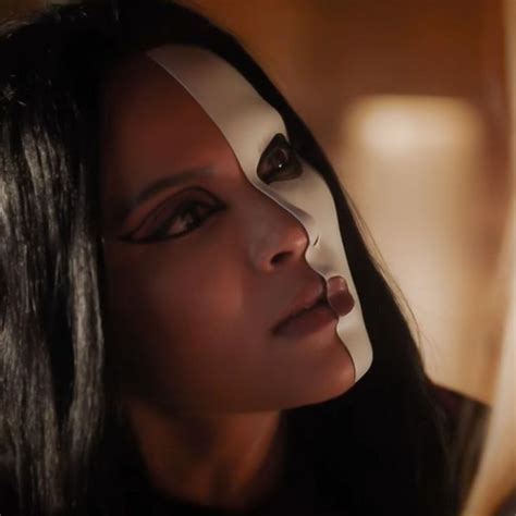 A Woman With Black Hair And White Face Paint Looks Into The Distance As